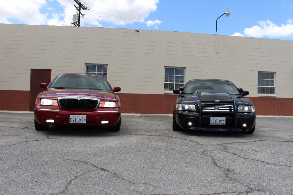 Red Mercury sedan and black Ford Crown Victoria parked front-on before a tan block building