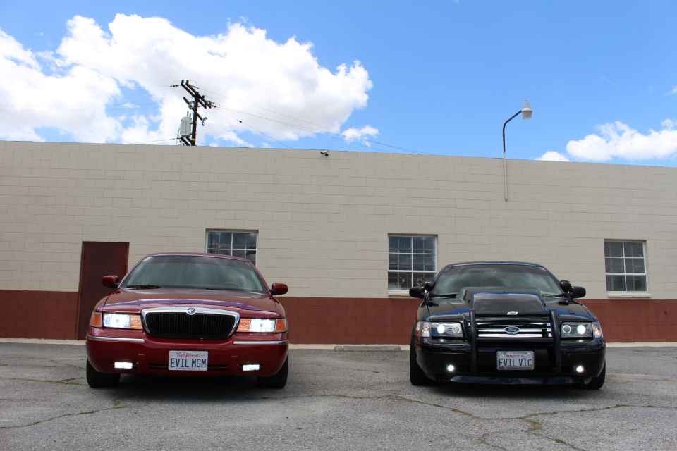 Maroon Mercury sedan and black Ford Crown Victoria parked front-on under a bright cloudy sky