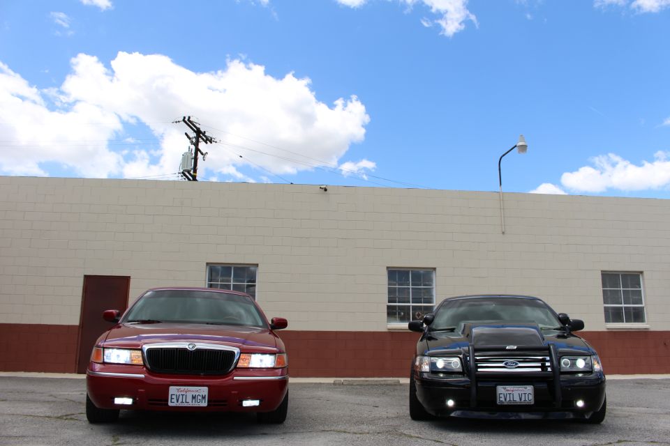 Red Mercury sedan and black Ford Crown Victoria parked front-on against a tan industrial wall