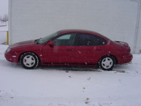 1998 Ford Taurus - A red 1998 Ford Taurus sedan is parked on a snowy surface, with snowflakes falling.