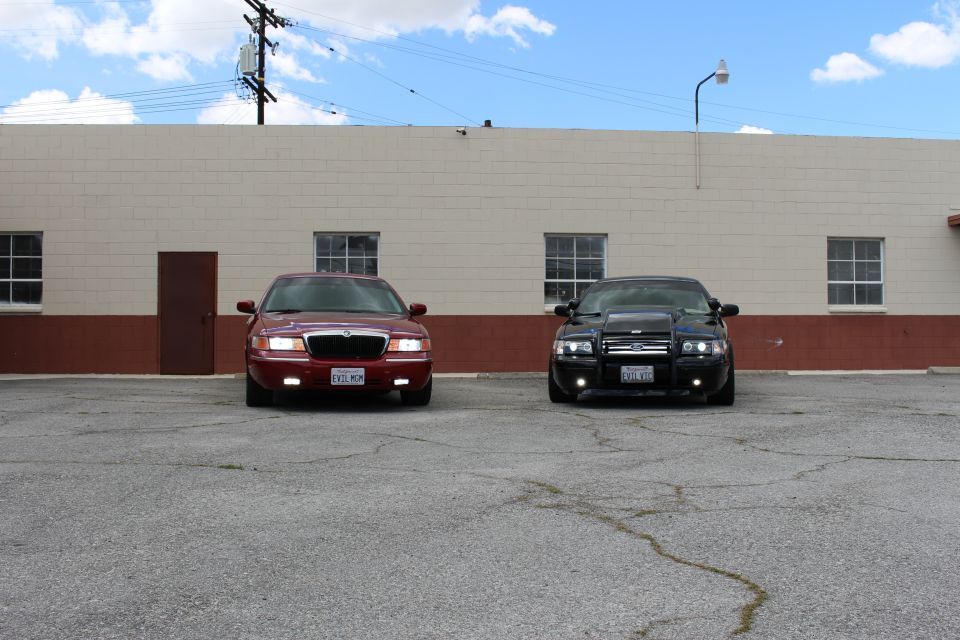 Maroon Mercury sedan and black sedan parked head-on in front of a warehouse