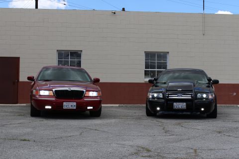 2003 Ford Crown Victoria - Close head-on view of a maroon Mercury reading EVIL MOM beside a black Ford with a push bar reading EVIL VIC.