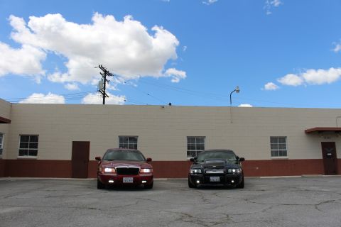 2003 Ford Crown Victoria - maroon Mercury and a black sedan face the camera on asphalt below a broad sky filled with white clouds.