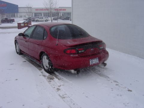 1998 Ford Taurus - A red 1998 Ford Taurus is parked in a snowy lot outside a strip mall.