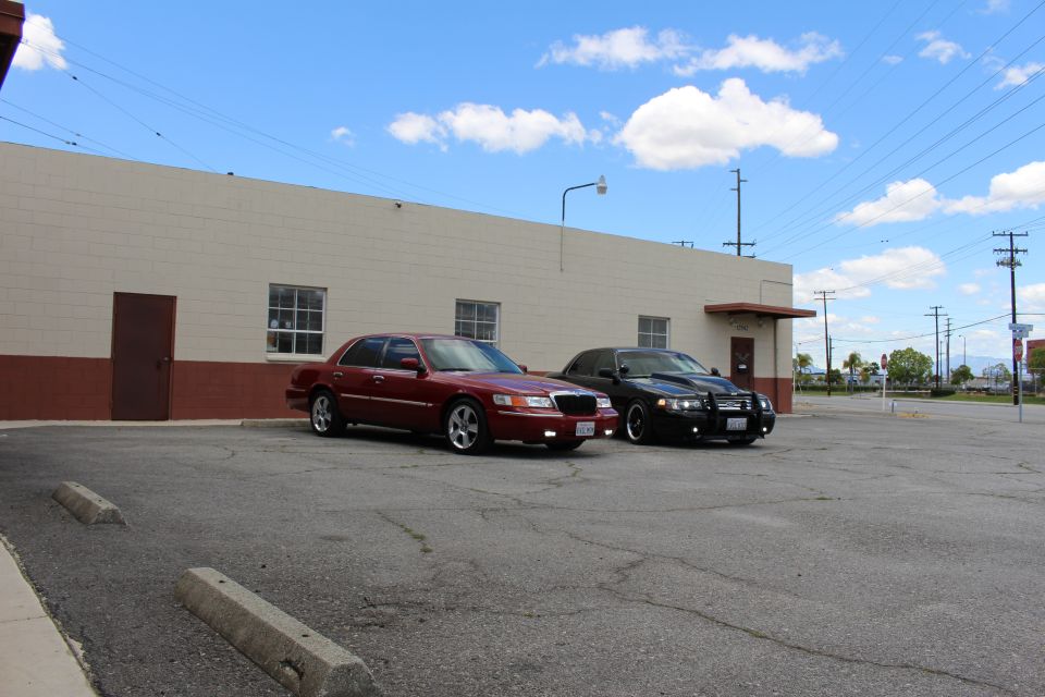 Wide view of maroon and black sedans parked beside a long warehouse