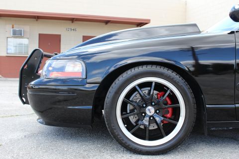 2003 Ford Crown Victoria - Close-up of a black sedan's front fender, black wheel with red brake caliper and a tubular push bumper, building in background.