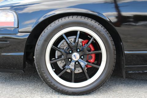 2003 Ford Crown Victoria - Tight close-up of a black multi-spoke wheel with polished lip and a red brake caliper on a black car.