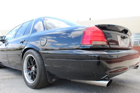 2003 Ford Crown Victoria - Low-angle rear corner view of a black sedan highlighting the red taillight, black multi-spoke wheel and chrome exhaust tip.