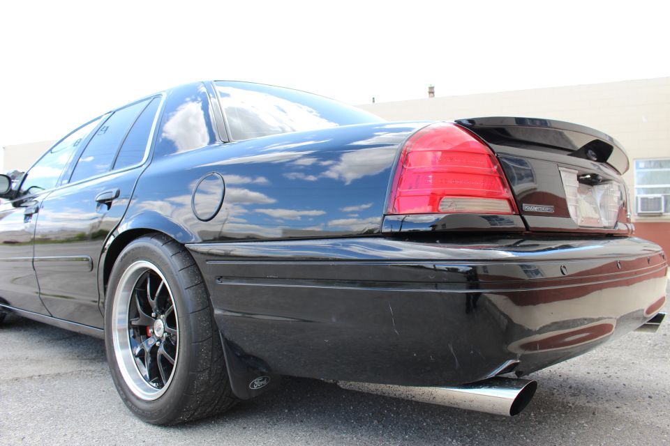 Low rear corner of a black sedan with taillight, black wheel and exhaust tip