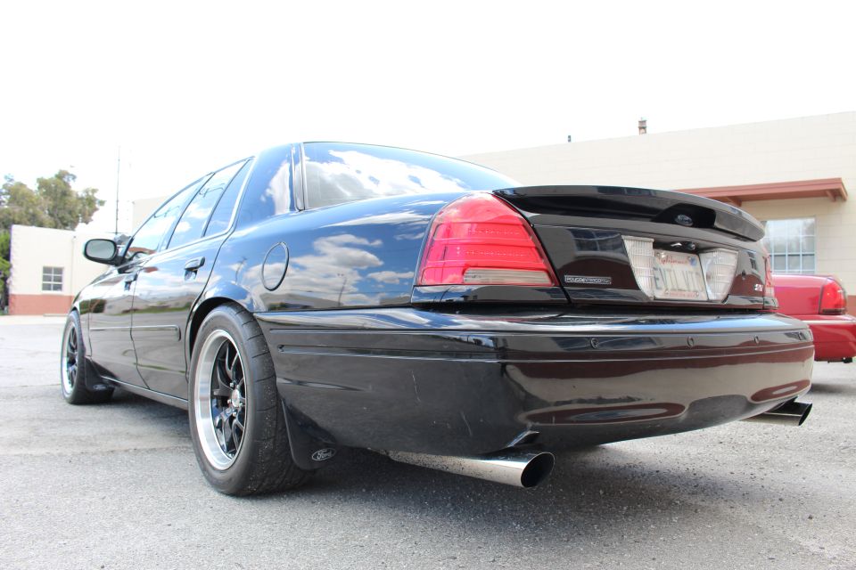 Rear three-quarter of a black sedan with rear spoiler and black wheels in a lot