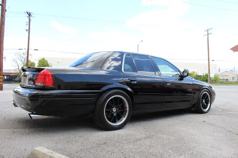 2003 Ford Crown Victoria - Rear three-quarter view of a lowered black sedan with a trunk spoiler and black wheels, power lines overhead.