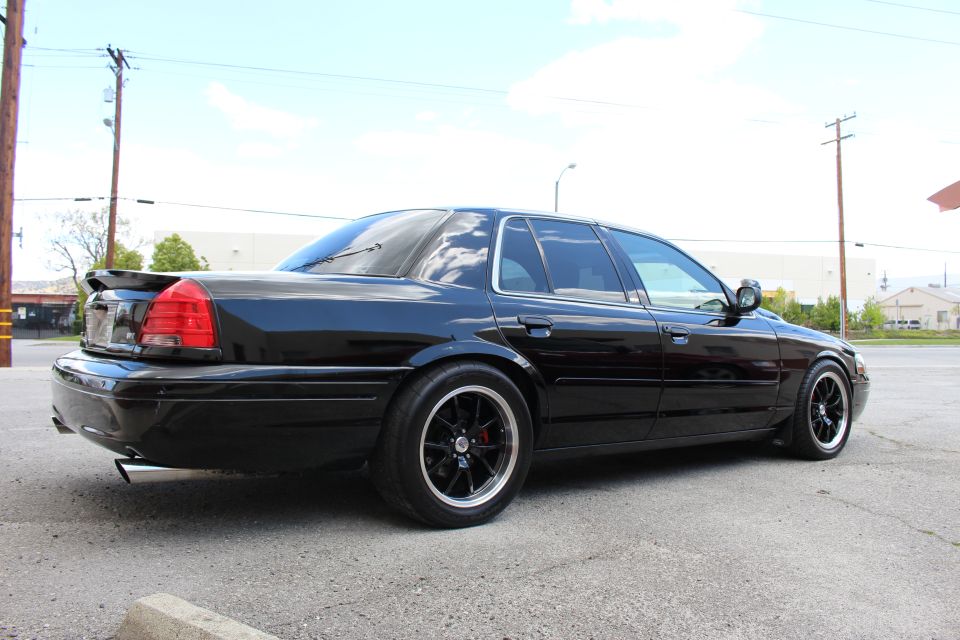 Rear three-quarter of a lowered black sedan with spoiler and black wheels, power lines