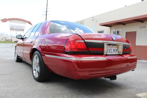 2003 Ford Crown Victoria - Rear three-quarter view of a dark red Mercury sedan with full-width taillights and a California EVIL MGM plate.