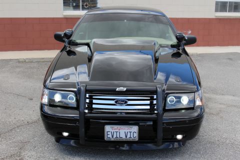 2003 Ford Crown Victoria - Head-on view of a black Ford sedan with a raised hood scoop, black push bumper and a California EVIL VIC plate.