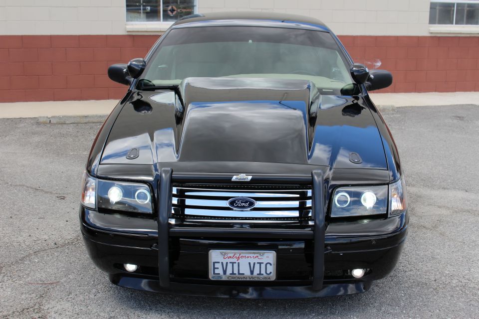 Front view of a black Ford with hood scoop, push bumper and EVIL VIC plate