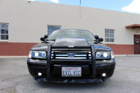 2003 Ford Crown Victoria - Head-on view of a black Ford sedan with halo headlights, hood scoop, black push bumper and California EVIL VIC plate.