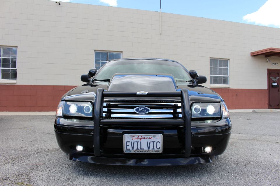 Front view of a black Ford sedan with push bumper, hood scoop and EVIL VIC plate