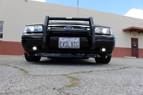 2003 Ford Crown Victoria - Low head-on shot of a black Ford sedan showing the Ford grille, push bumper, halo lights and a California EVIL VIC plate.