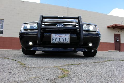 2003 Ford Crown Victoria - Low head-on view of a black Ford sedan with a push bumper, Ford grille, halo headlights and a California EVIL VIC plate.
