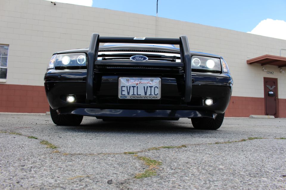 Low front view of a black Ford sedan with Ford grille, push bumper, EVIL VIC plate