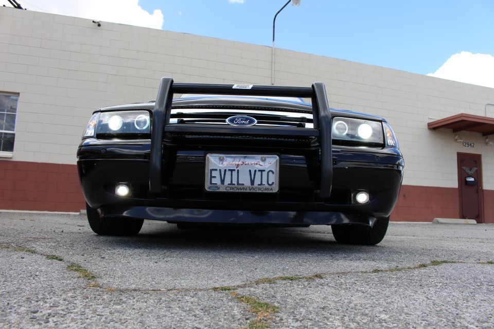 Low front view of a black Ford sedan with push bumper, halo lights, EVIL VIC plate