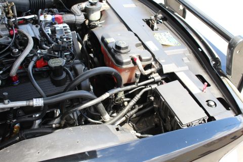 2003 Ford Crown Victoria - Detail of a black car's engine bay showing the coolant overflow tank, wiring harness and an open fuse box.