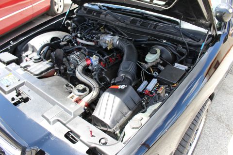 2003 Ford Crown Victoria - Engine bay of a dark sedan fitted with a K&N cone air filter and aftermarket intake, with a red car parked in the background.