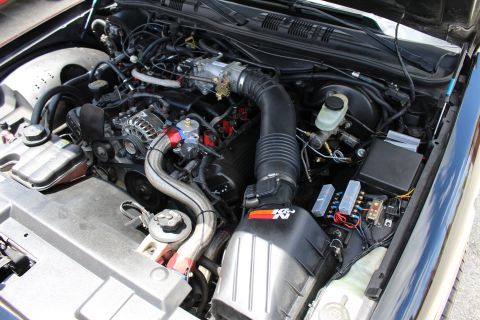 2003 Ford Crown Victoria - Detailed engine bay showing a K&N cone air filter, accordion intake tube and fuse box of a modified sedan.