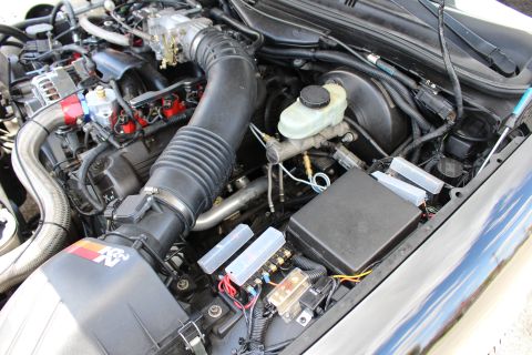 2003 Ford Crown Victoria - Engine compartment showing a large ribbed air intake hose, K&N filter, brake master cylinder and an open fuse box.