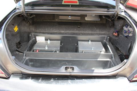 2003 Ford Crown Victoria - Car trunk fitted with a metal tray holding two aluminum battery boxes and audio amplifier wiring along the sides.