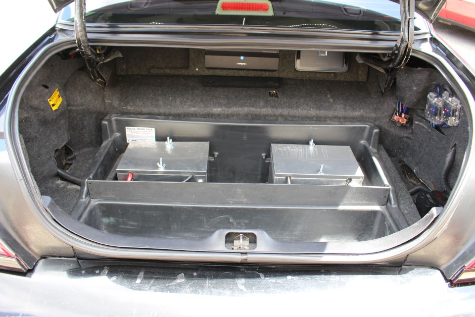 Open car trunk with two metal battery boxes and amplifier wiring
