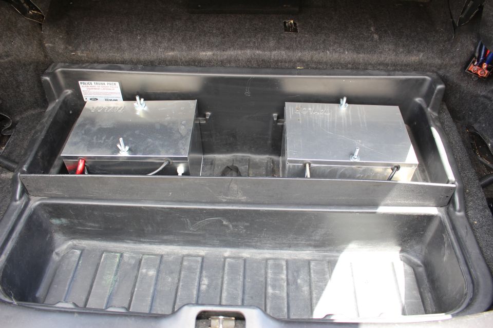 Trunk tray holding two aluminum battery boxes with a Ford police label