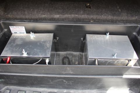 2003 Ford Crown Victoria - Two aluminum battery boxes secured with wing nuts in a black trunk tray bearing a Ford police pack label.