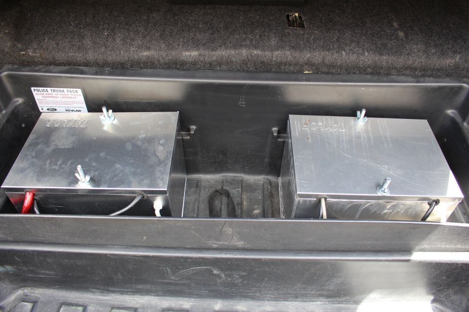 Two aluminum battery boxes mounted in a trunk tray with wing nuts