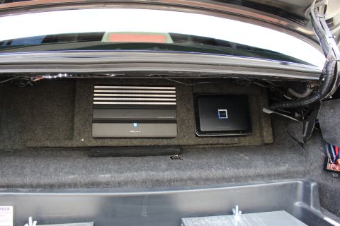 2003 Ford Crown Victoria - Trunk audio install showing two amplifiers, one finned, mounted on a carpeted board above battery boxes.