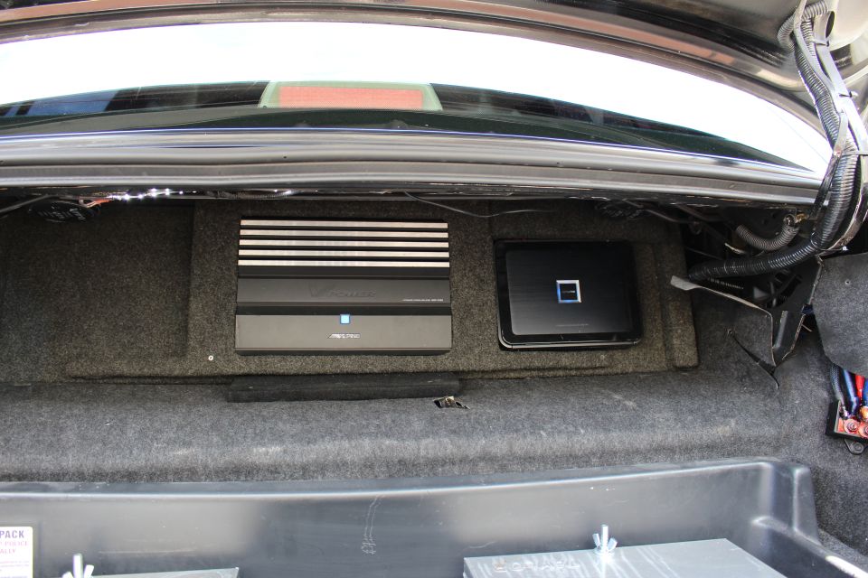 Two car audio amplifiers mounted on carpeted board in a trunk
