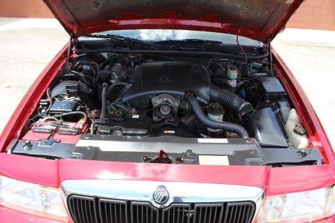2003 Ford Crown Victoria - Open engine bay of a red Mercury sedan with a black plastic engine cover and the Mercury emblem visible on the grille.