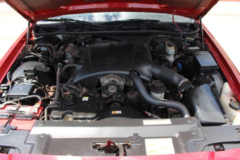 2003 Ford Crown Victoria - Engine bay of a red sedan showing a central black engine cover, serpentine belt pulleys and air intake.