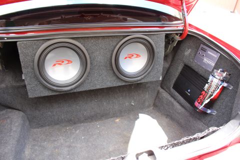 2003 Ford Crown Victoria - Trunk audio install showing two subwoofers in a carpeted box, an amplifier and coiled cabling inside a red car.