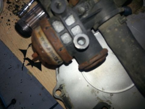 1994 Ford Bronco - Close-up of a rusty automotive part, possibly a vacuum actuator, on a wooden surface.