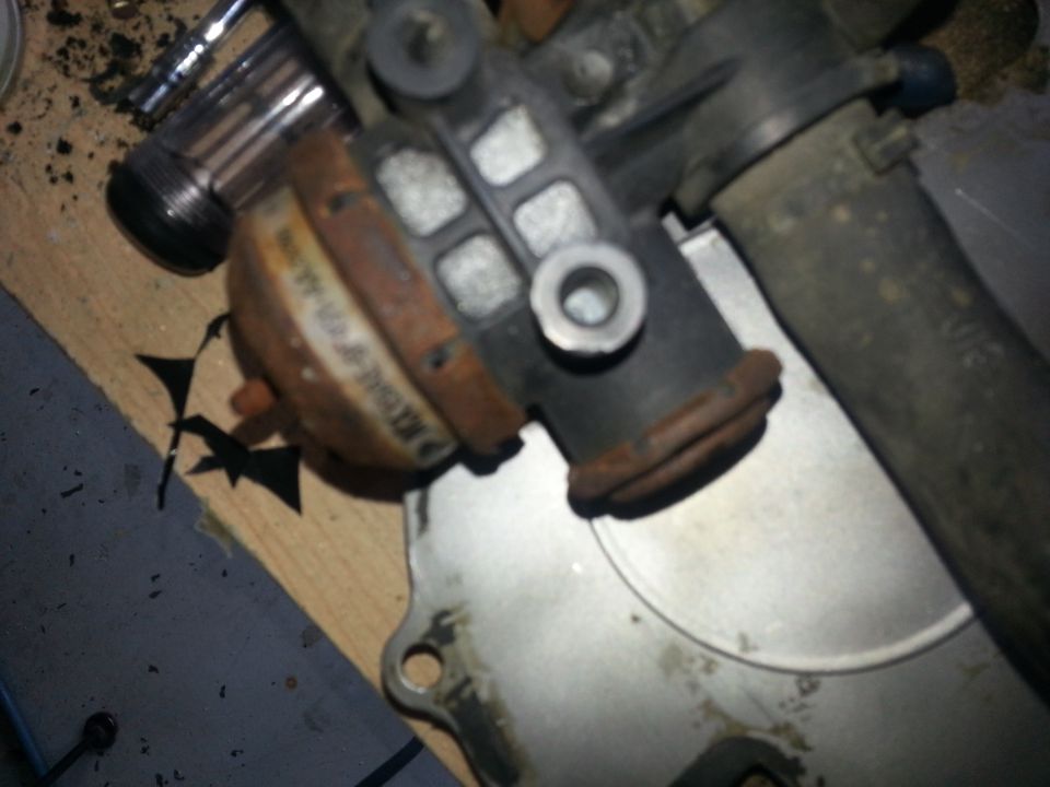 Close-up of a rusty automotive part, possibly a vacuum actuator, on a wooden surface