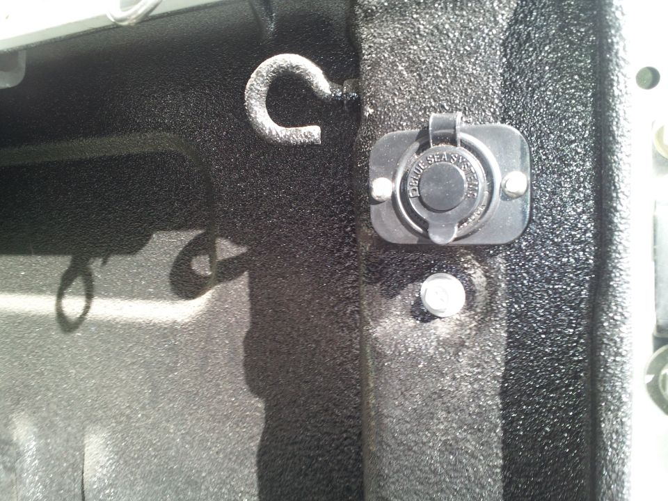 Close up of a truck bed showing a tie-down loop and a 12V power outlet labeled 'Blue Sea Systems'