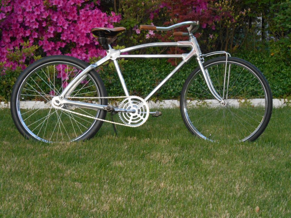 Chrome bicycle with brown leather seat and handlebars, parked on grass in front of pink flowers