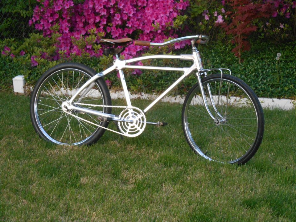 Chrome bicycle with brown leather seat and handlebars, parked on grass in front of pink flowers