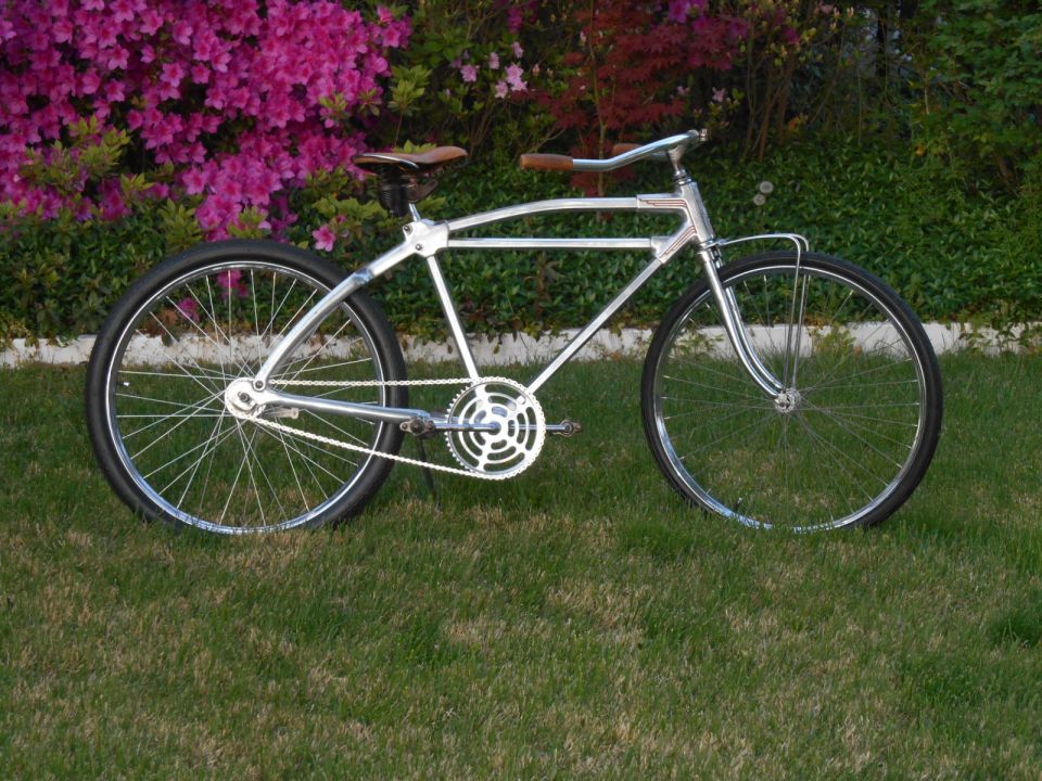 Chrome bicycle with brown leather seat and handlebars parked on grass with pink flowers