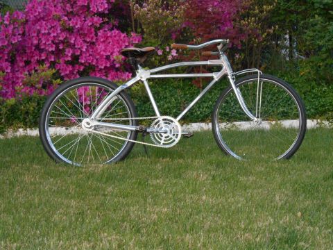 Chrome cruiser bicycle with brown grips and saddle, parked on grass with pink azaleas