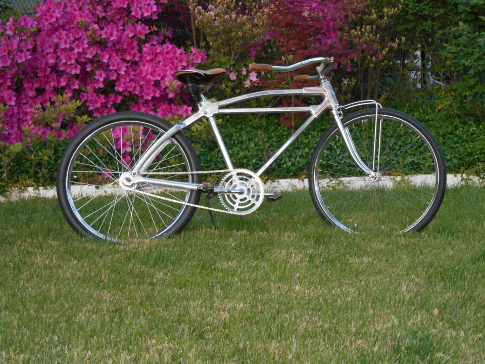 Chrome cruiser bicycle with brown grips and saddle, parked on grass with pink azaleas