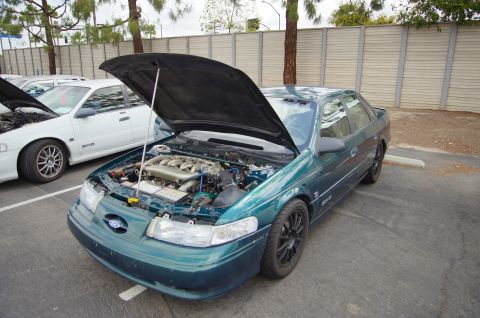 1995 Ford Taurus - A green sedan with its hood open is parked in a lot next to another vehicle.
