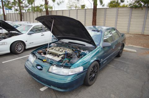 1995 Ford Taurus - A green Ford Taurus from the mid-1990s is displayed with its hood open, revealing the engine compartment.