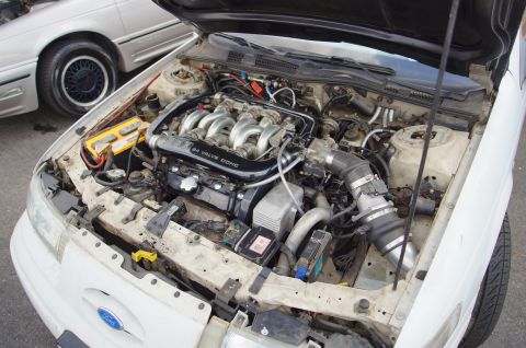 1995 Ford Taurus - Engine bay of a white car, a Ford SHO V6 24 valve DOHC engine. Another vehicle is partially visible.